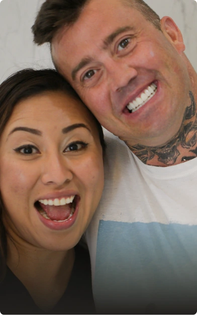 A happy couple smiling brightly, showing off the natural-looking final dental crown and smile makeover results.