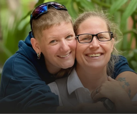 Two happy women smiling together outdoors, showcasing the natural results of a Full Mouth Restoration.